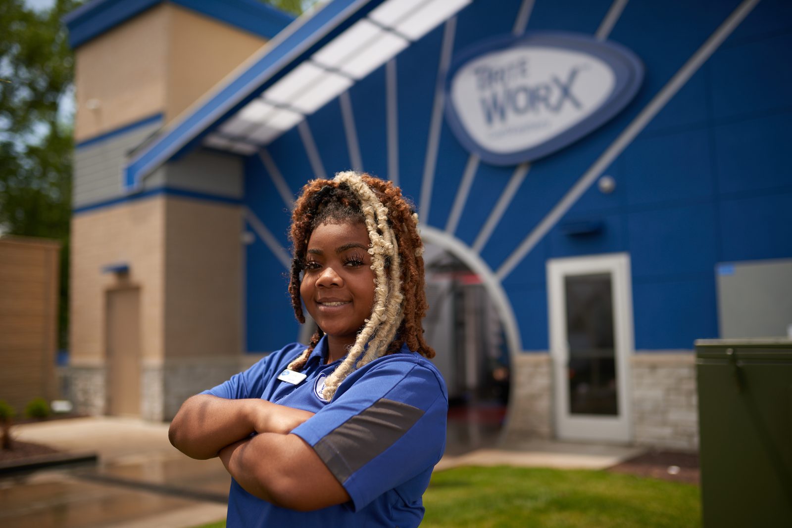 A Brite WorX team member standing with arms folded outside one of the stores, the blue building and its arch behind her