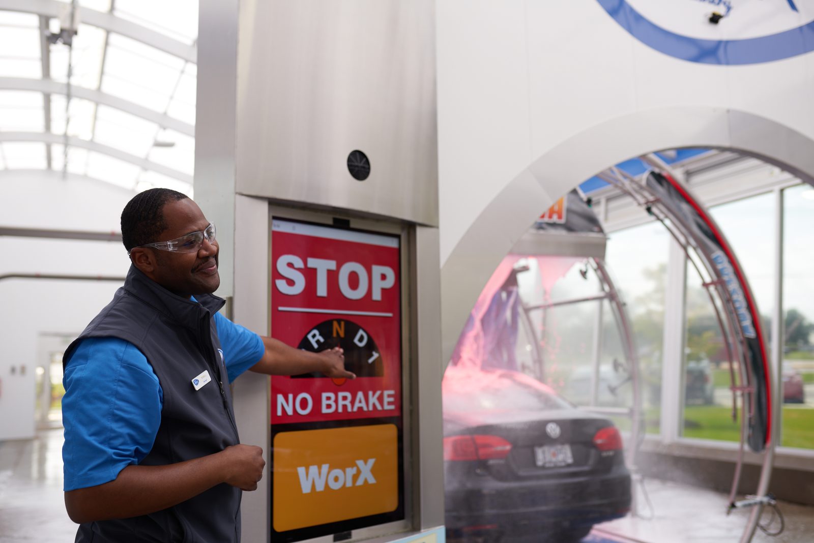 A Brite WorX attendant at the entry kiosk, a car moving into the wash tunnel behind him