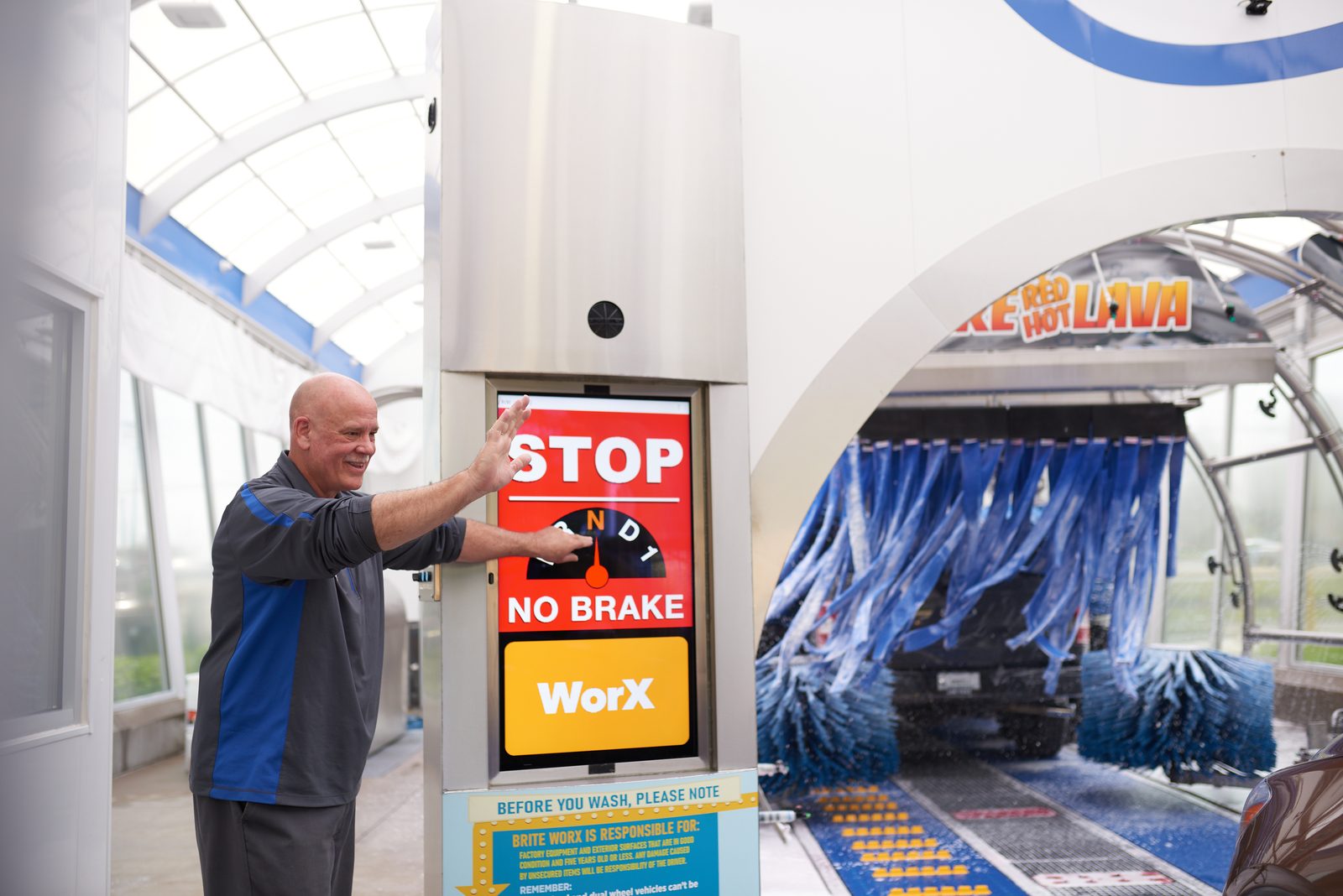 A Brite WorX attendant guiding a driver at the tunnel entry kiosk, the STOP and NO BRAKE screen beside him
