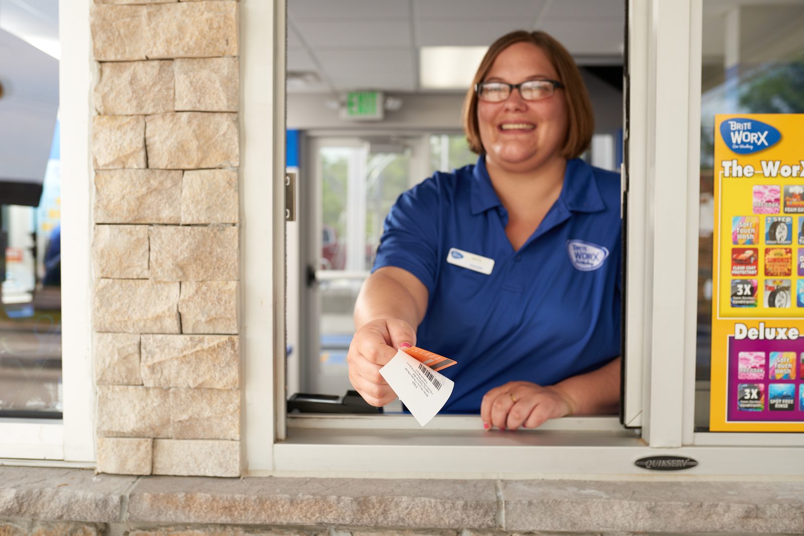 A Brite WorX team member leaning out of the pay window, handing over a receipt and a wash card