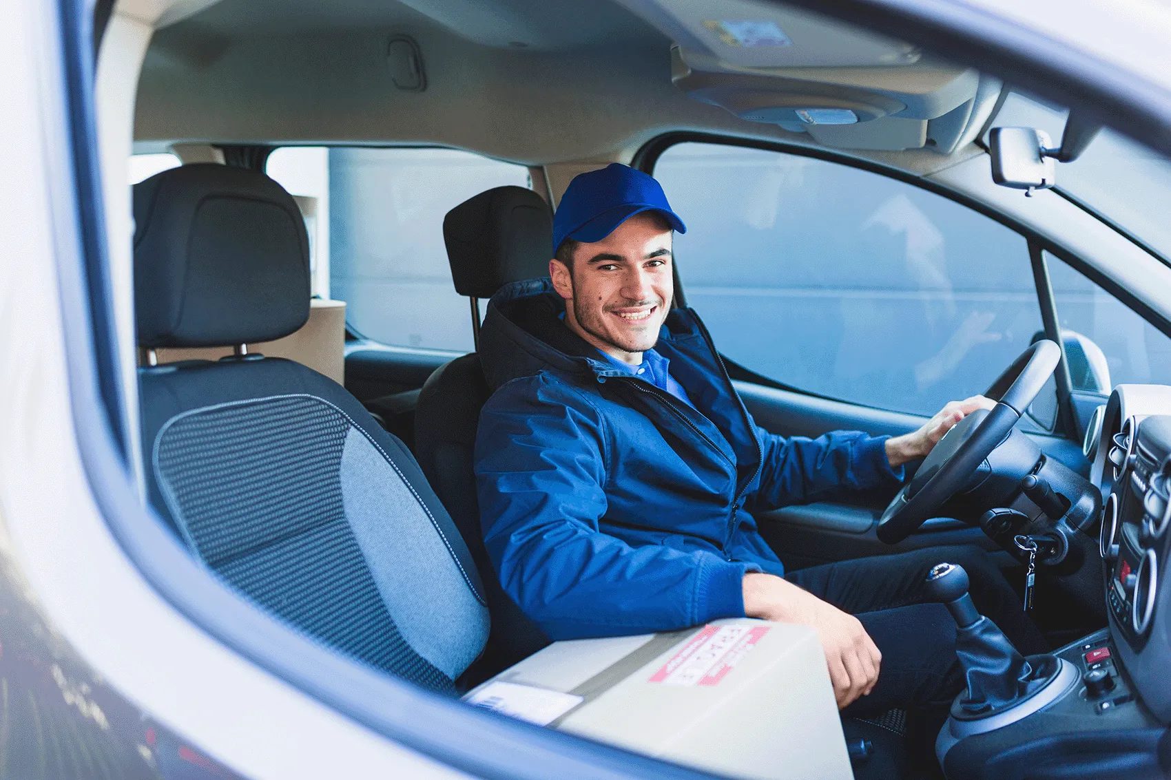 A driver in a Brite WorX blue jacket and cap at the wheel of a clean delivery van, a parcel on the seat beside him