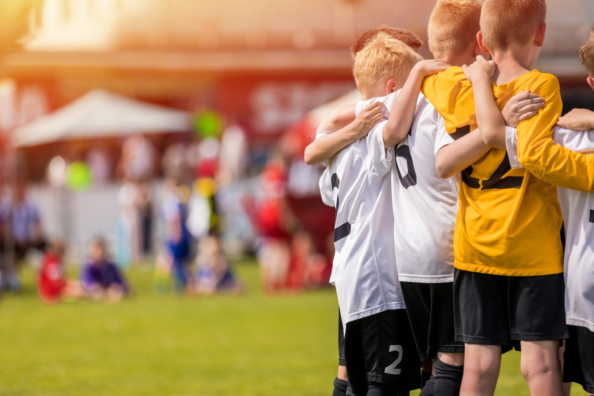 A youth sports team huddled arm in arm on the touchline